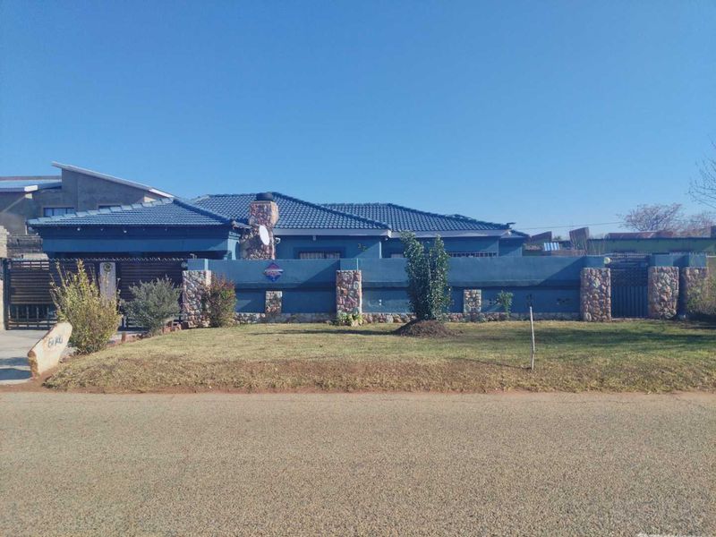 Front elevation of a residential property featuring a blue painted facade, stone-clad boundary wall, and a tiled roof.