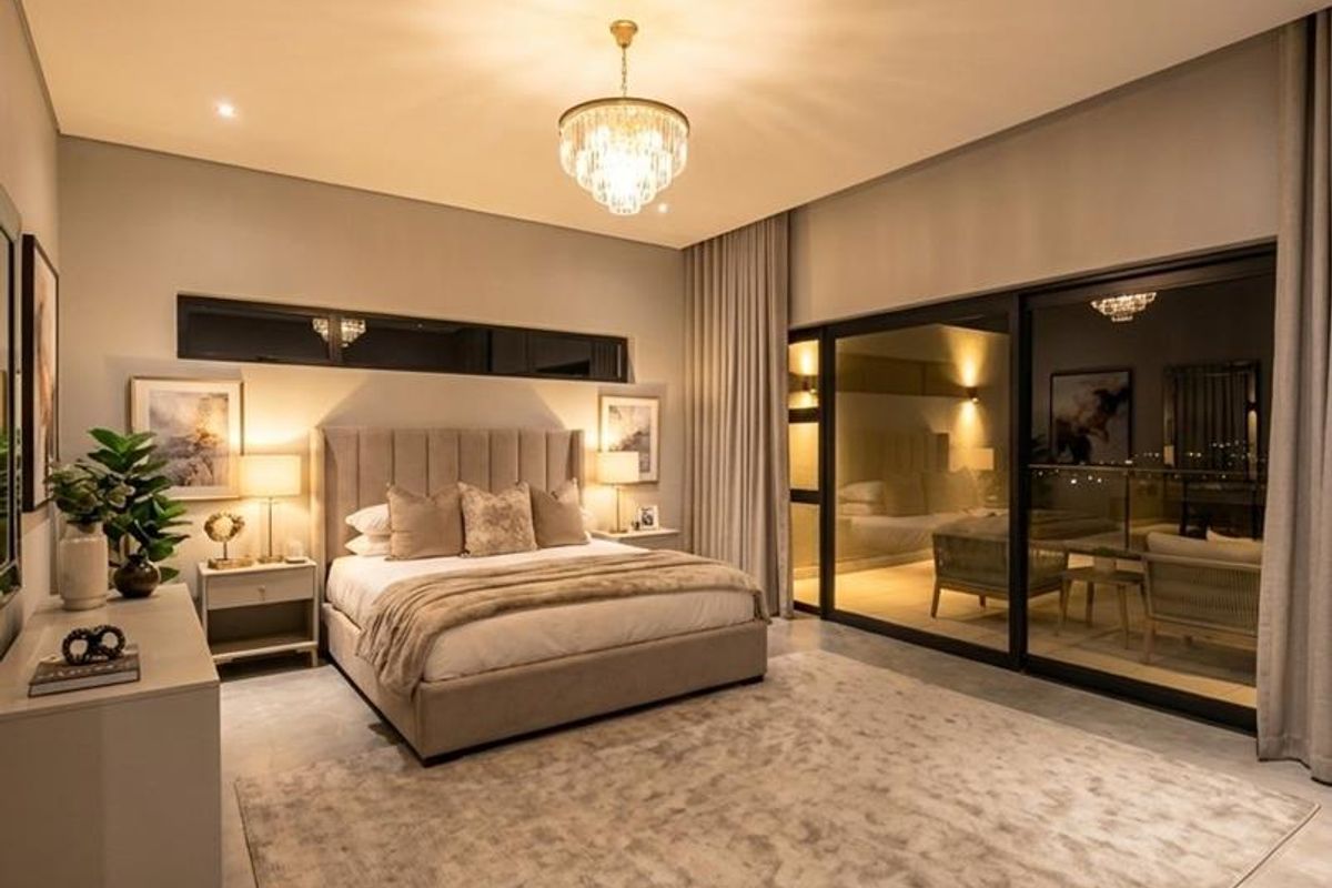 A spacious, modern bedroom featuring high ceilings, elegant crystal chandelier lighting, large sliding glass doors, and premium tiled flooring.