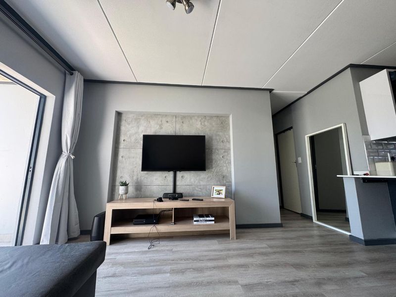 Modern open-plan living area featuring a concrete accent wall with a recessed TV mount, laminate flooring, and direct access to an outdoor space.