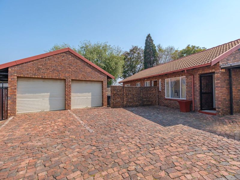 Front exterior view of a townhouse featuring a double garage, brick paved driveway, and classic facebrick facade with a tiled roof.