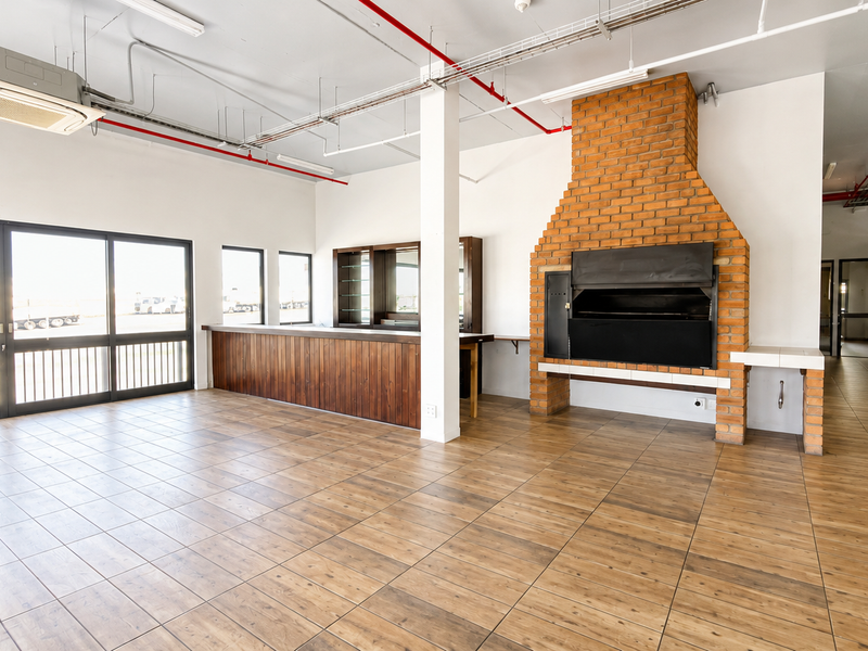 Spacious open-plan industrial area featuring a built-in brick fireplace, wooden bar counter, tiled flooring, and exposed ceiling infrastructure with integrated air conditioning.