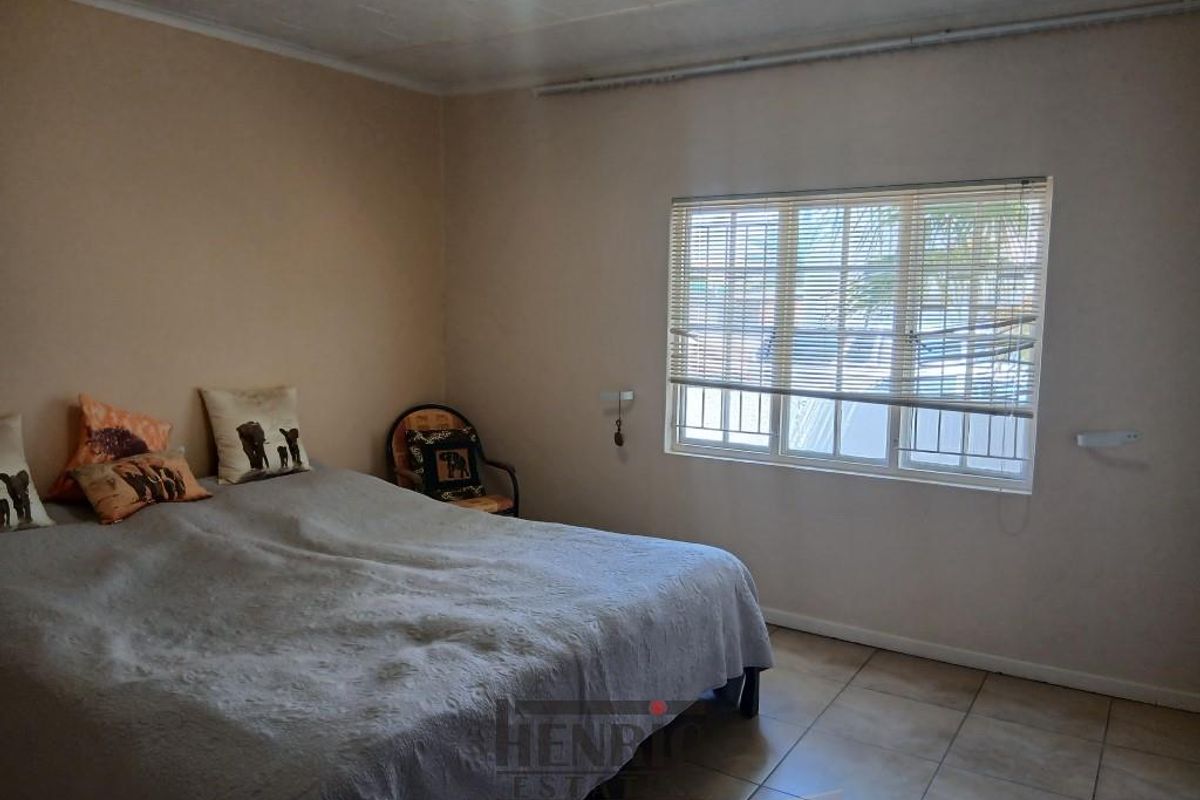 A functional bedroom featuring tiled flooring and a window fitted with horizontal blinds, providing natural light and a view of the exterior.
