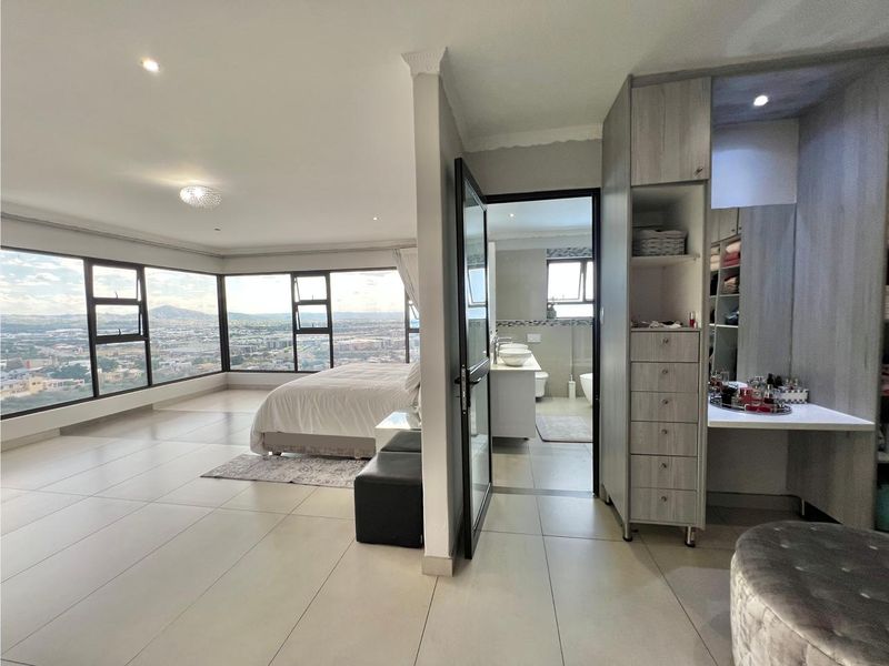 Spacious master bedroom featuring large format floor tiles, extensive built-in cabinetry, and expansive windows offering panoramic city views with an adjoining en-suite bathroom.