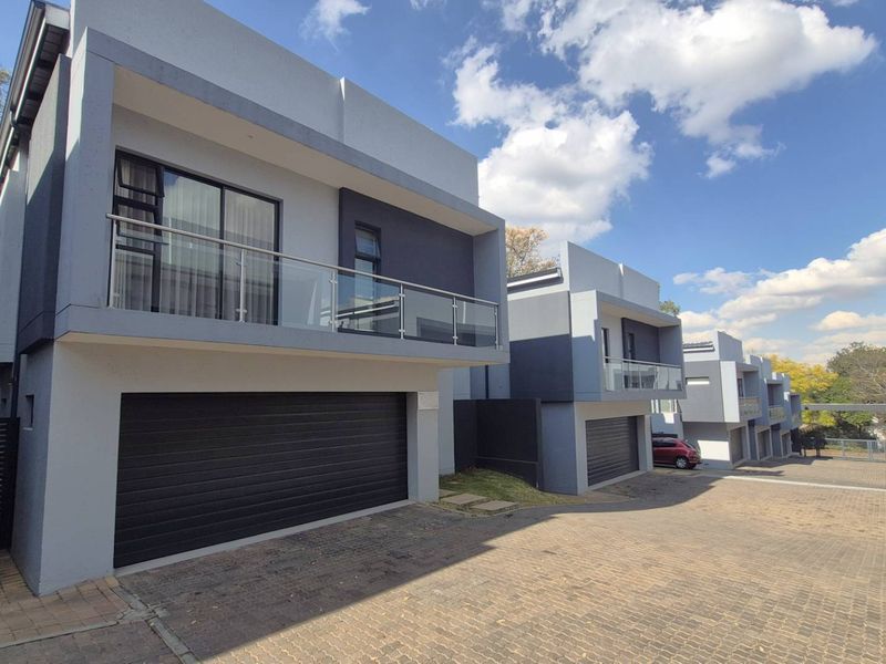 Modern cluster home exterior featuring a double garage, paved driveway, and an upper-level balcony with glass balustrades.