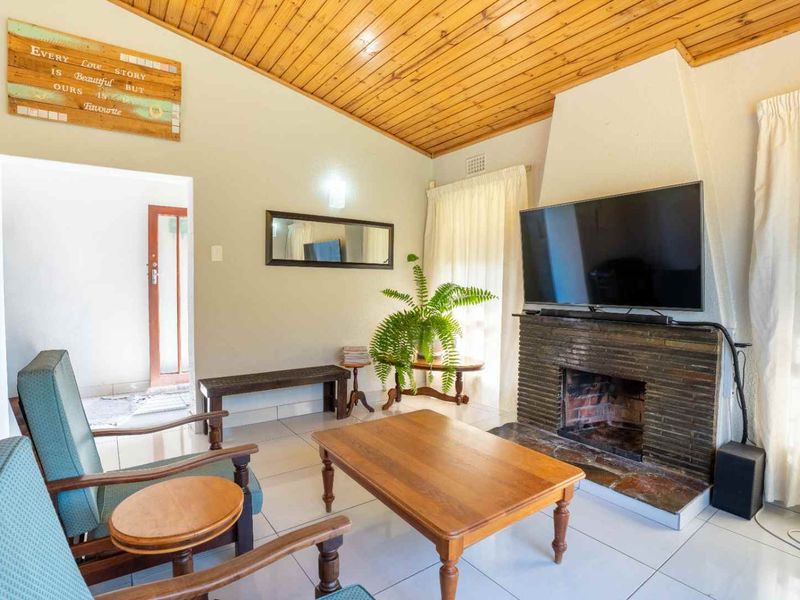 A cozy living room featuring a stone fireplace, tiled flooring, and a warm timber tongue and groove ceiling.