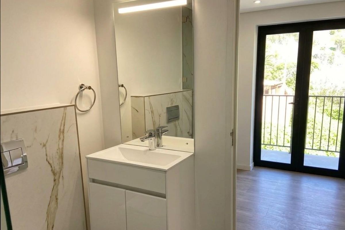 Modern bathroom featuring a sleek vanity with integrated basin, wall-mounted mirror with lighting, and marble-effect wall tiling, adjacent to a balcony entrance.