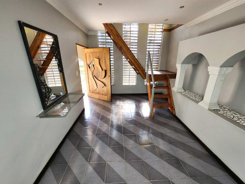 Spacious entrance hall featuring a wooden staircase, decorative arched wall niches, glass block windows, and patterned tiled flooring.