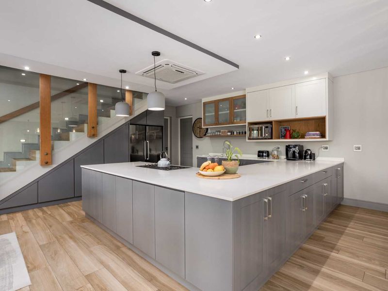 Modern kitchen featuring a large central island with quartz countertops, sleek grey cabinetry, integrated appliances, and clever under-stair storage integration.