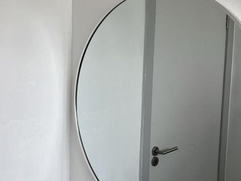 A clean bathroom vanity area featuring a modern basin, chrome mixer tap, tiled splashback, and a circular wall-mounted mirror.