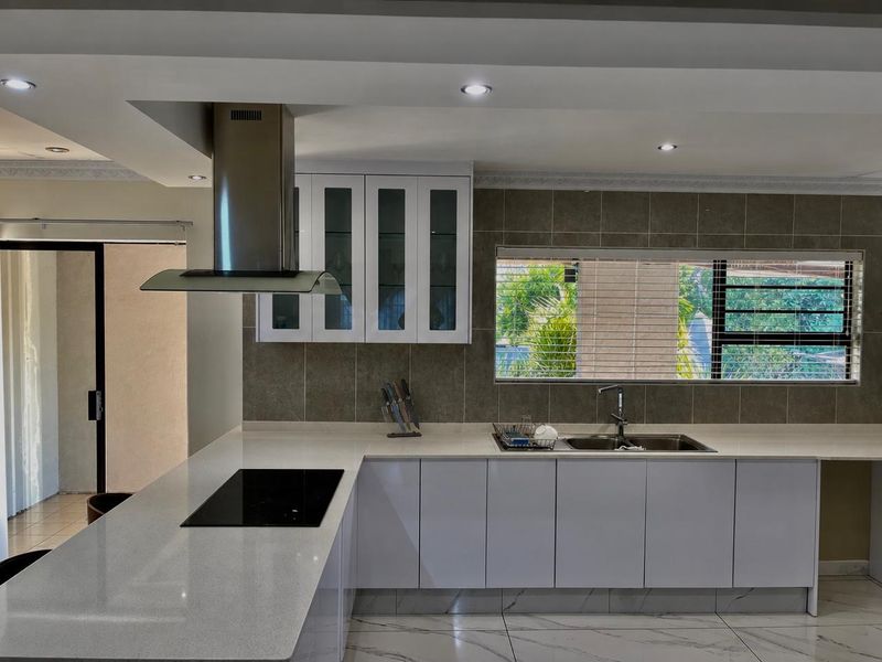 Modern kitchen featuring sleek white cabinetry, quartz countertops, a built-in induction hob with stainless steel extractor, and elegant marble-look floor tiles.