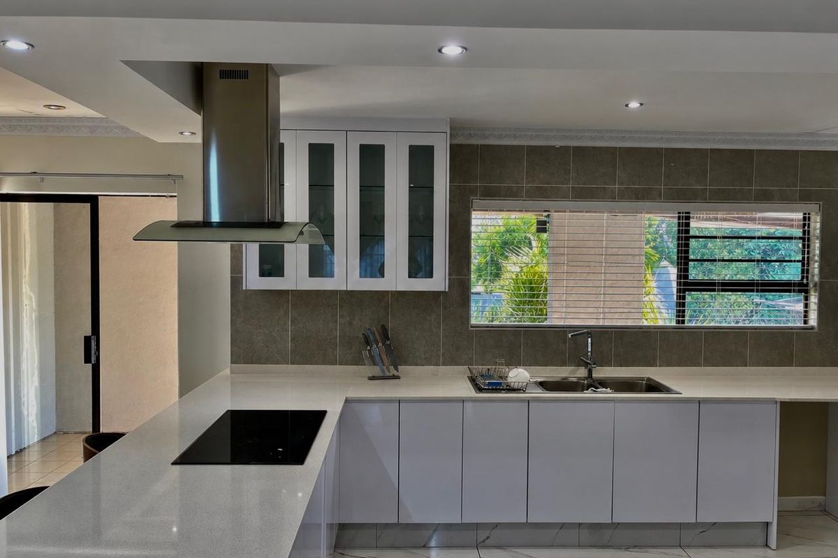 Modern kitchen featuring sleek white cabinetry, quartz countertops, a built-in induction hob with stainless steel extractor, and elegant marble-look floor tiles.