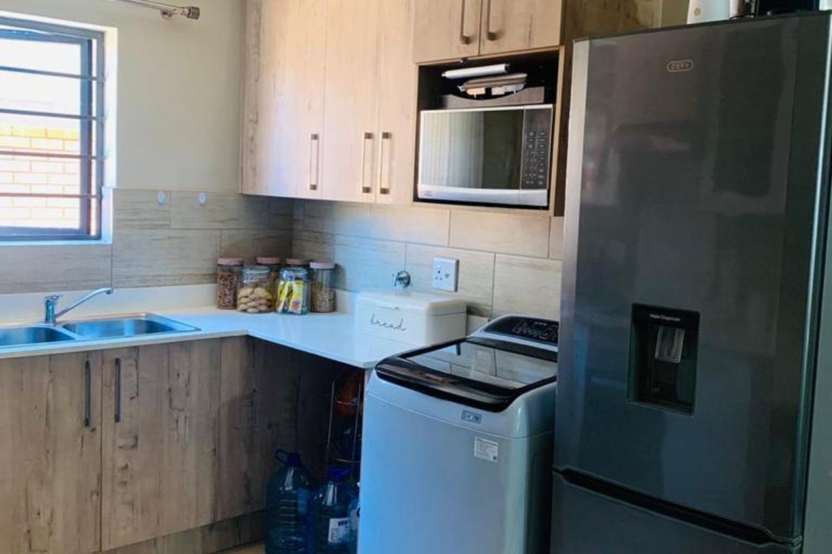 A functional kitchen featuring light wood-grain cabinetry, tiled backsplash, double stainless steel sink, and dedicated space for a washing machine and refrigerator.