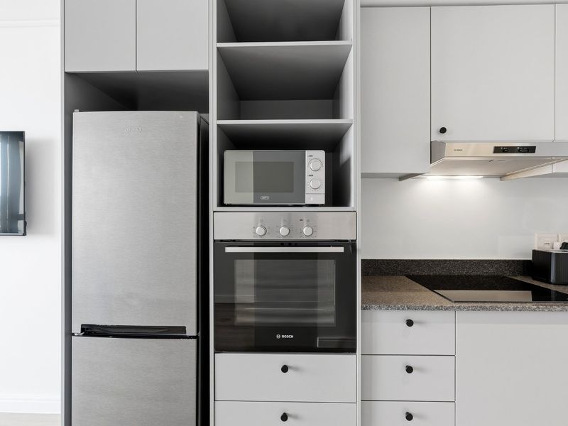 Modern kitchen featuring sleek grey cabinetry, stone countertops, integrated appliances including an oven, hob, and extractor fan, with dedicated microwave storage.