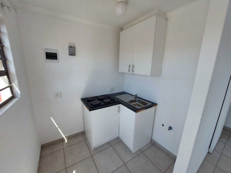 Compact kitchen area featuring white cabinetry, a built-in electric hob, a stainless steel sink, and tiled flooring.