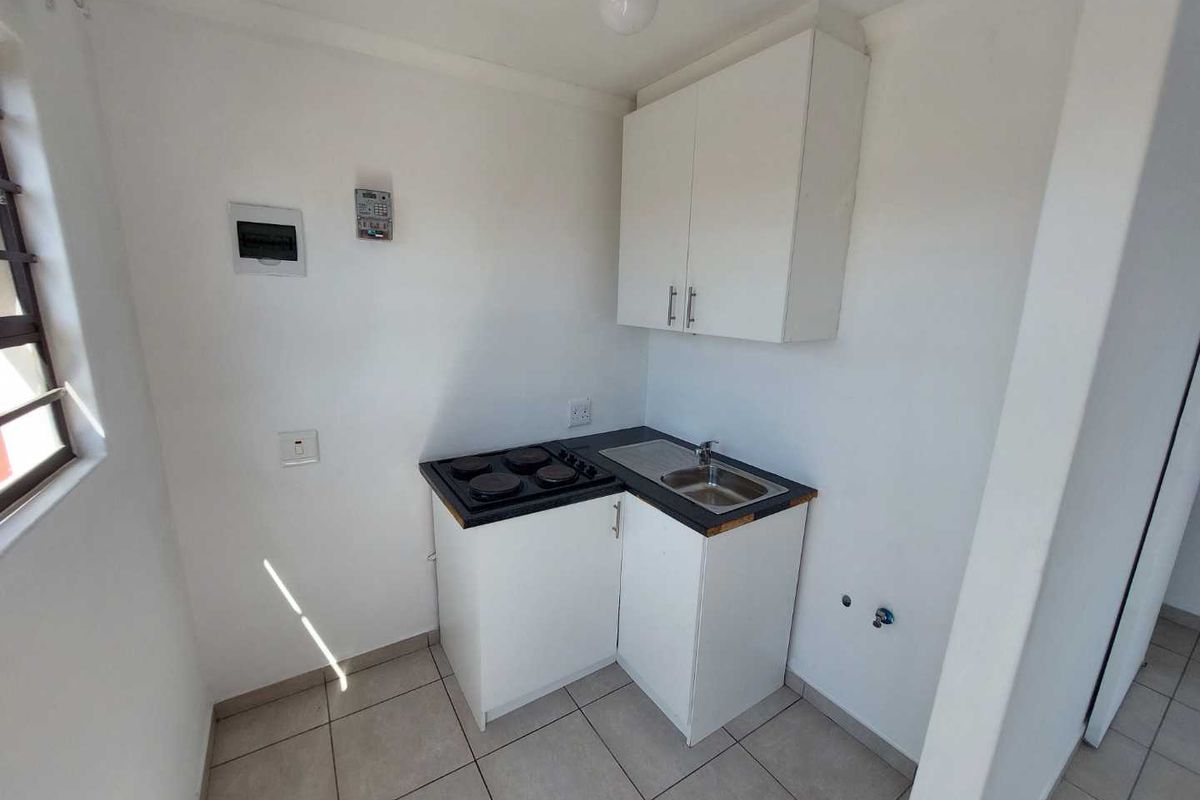 Compact kitchen area featuring white cabinetry, a built-in electric hob, a stainless steel sink, and tiled flooring.