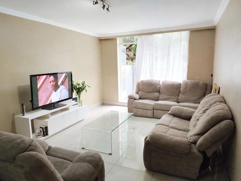 A comfortable living room featuring neutral wall tones, polished tiled flooring, and a sliding glass door providing natural light and garden access.