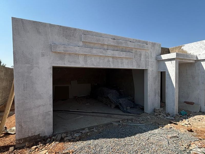 Exterior view of a garage under construction, featuring a plastered facade and open entrance, currently in the early stages of development.