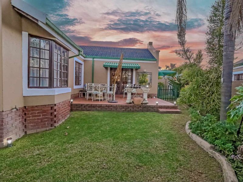 A well-maintained rear exterior view featuring a brick patio, landscaped garden, and classic bay window under a sunset sky.