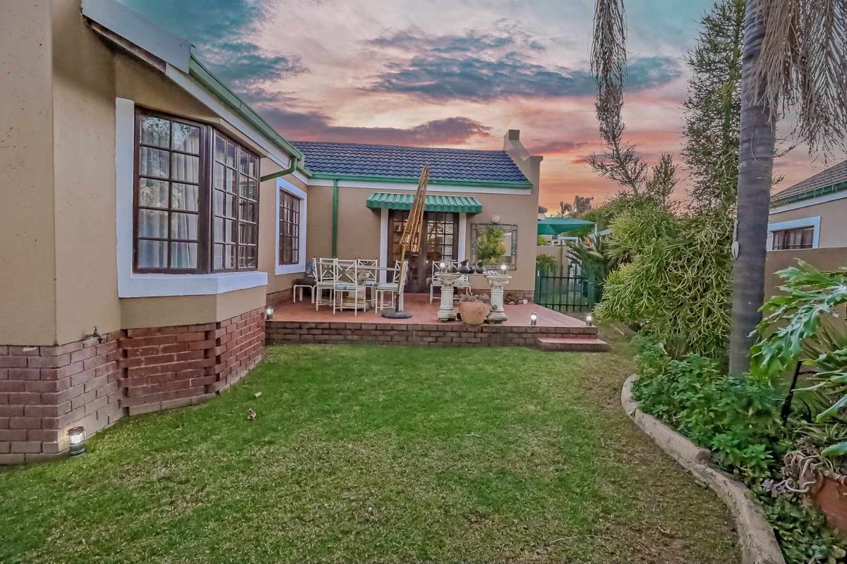 A well-maintained rear exterior view featuring a brick patio, landscaped garden, and classic bay window under a sunset sky.