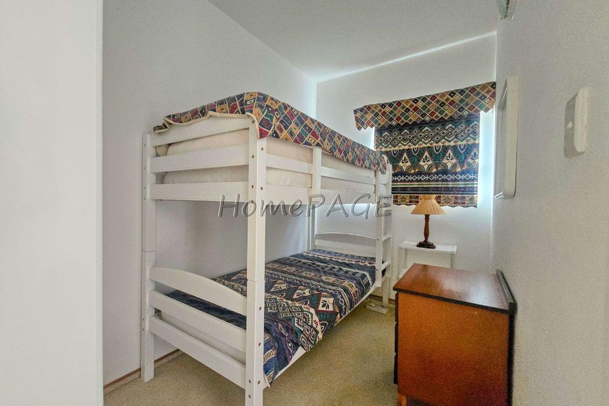 A compact bedroom featuring neutral carpeting and a window with a patterned roller blind.