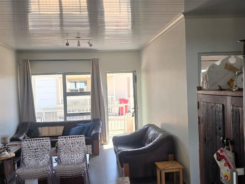 A living room area featuring tiled floors, glossy ceiling panels, and a sliding glass door providing access to the exterior.