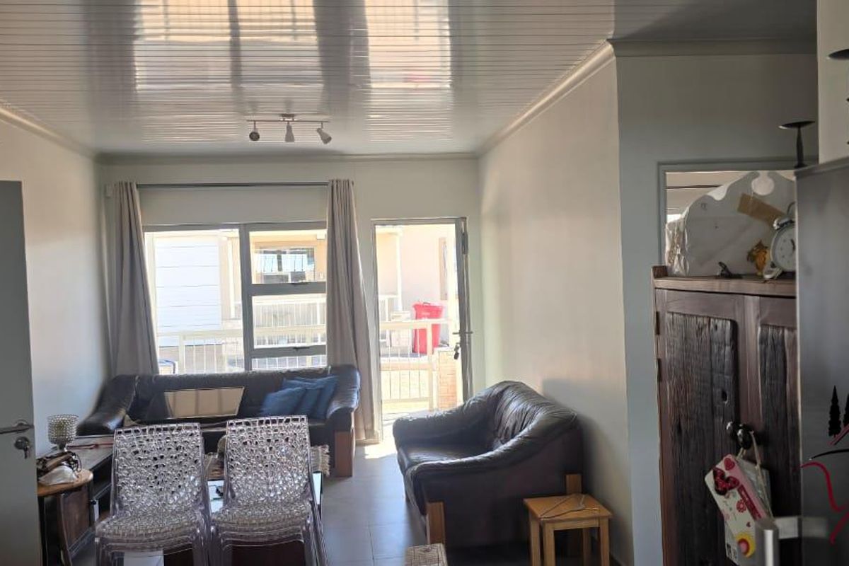 A living room area featuring tiled floors, glossy ceiling panels, and a sliding glass door providing access to the exterior.