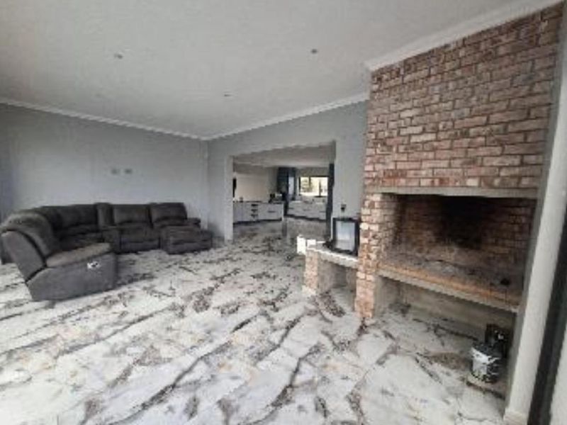 Spacious open-plan living area featuring a prominent exposed brick fireplace and distinctive marble-look tiled flooring, leading through to the kitchen area.