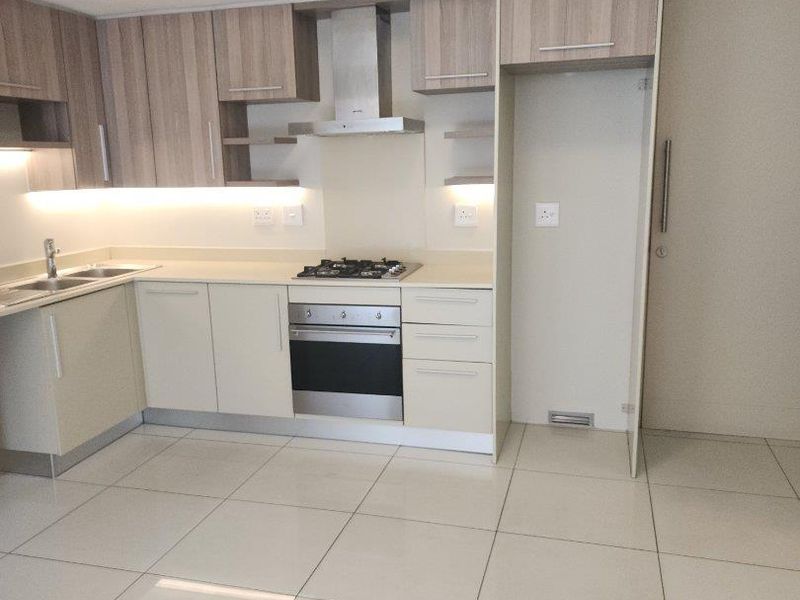 Modern kitchen featuring light wood-tone cabinetry, stainless steel built-in oven, gas cooktop, extractor fan, and sleek tiled flooring in an open-plan layout.