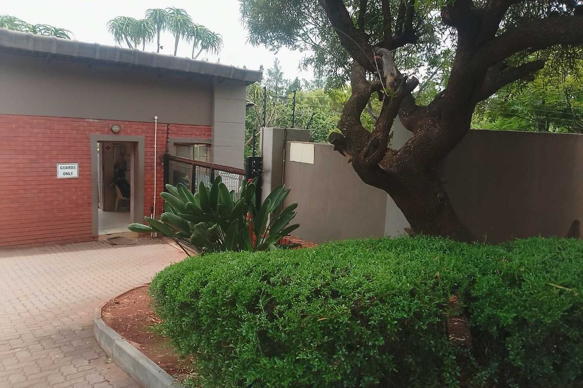 Exterior view of the property entrance featuring a brick facade, paved driveway, and established garden area with security fencing.