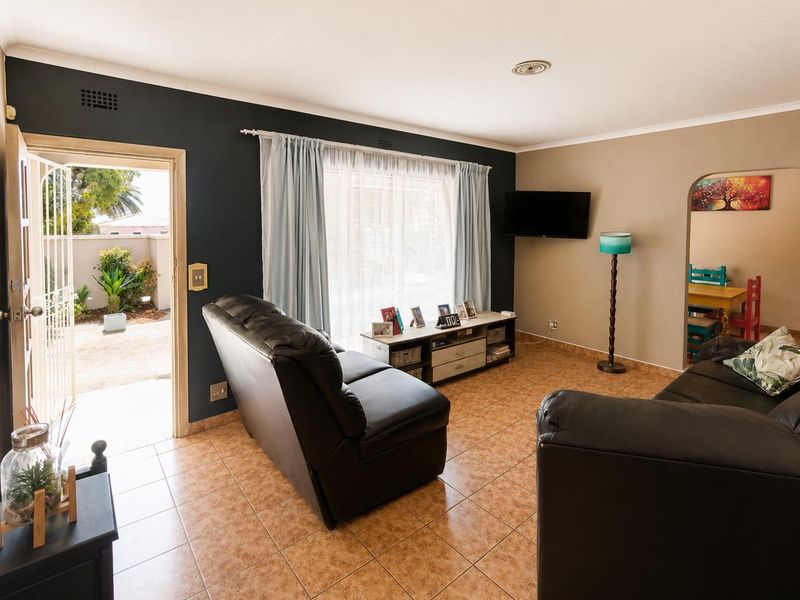 A living room featuring tiled flooring, a dark accent wall, and an arched doorway leading to an adjacent space, with direct access to the exterior.