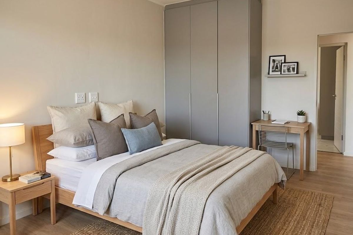 A well-maintained bedroom featuring neutral tones, light wood-look flooring, and a modern built-in wardrobe with sleek grey cabinetry.