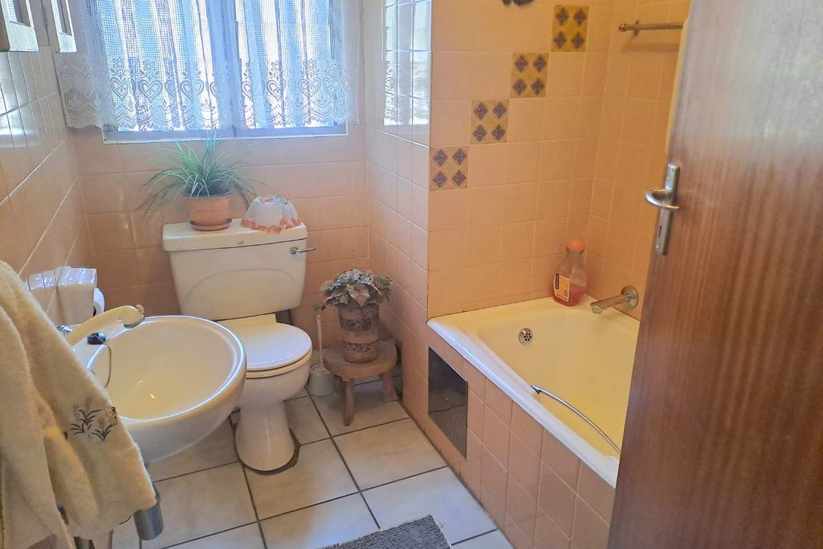 A dated bathroom featuring a built-in bathtub, pedestal basin, and toilet, finished with peach-toned wall tiles and white floor tiles.