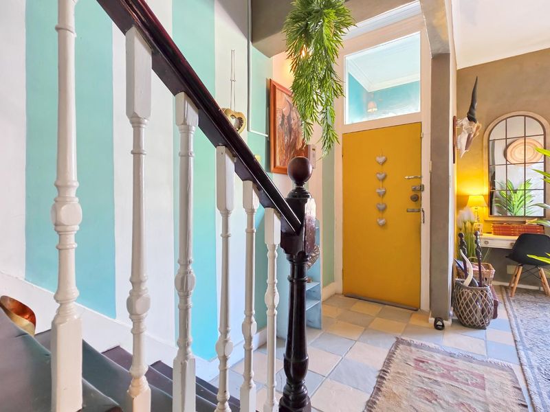 Welcoming entrance hall featuring a classic timber staircase, tiled flooring, and a bright yellow front door with a transom window.