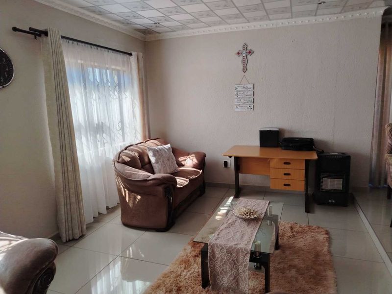 A living room featuring tiled flooring and a drop ceiling, with natural light entering through a window fitted with security bars.