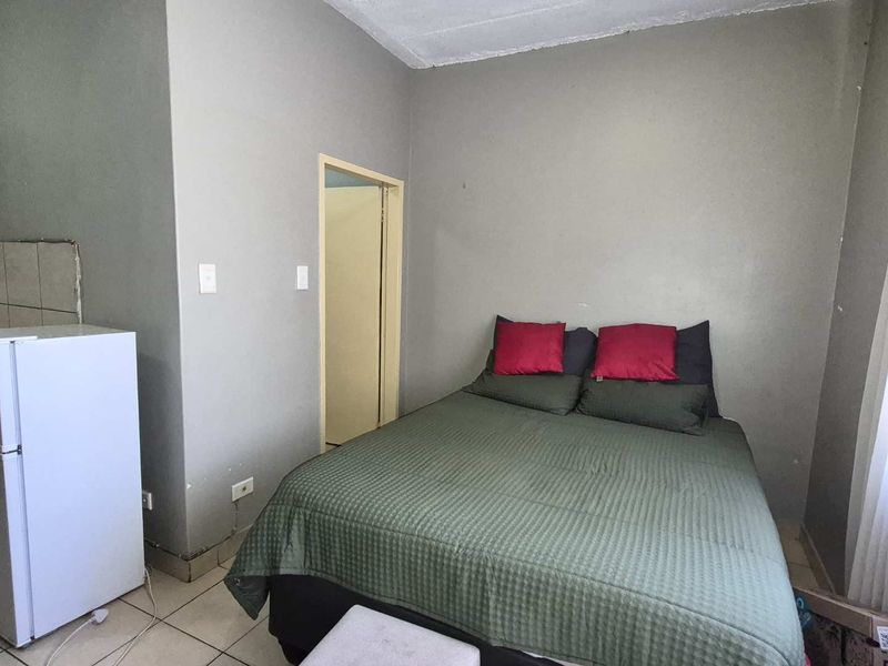 A compact bedroom featuring tiled flooring and neutral wall finishes, providing a functional space with direct access to an adjoining room.