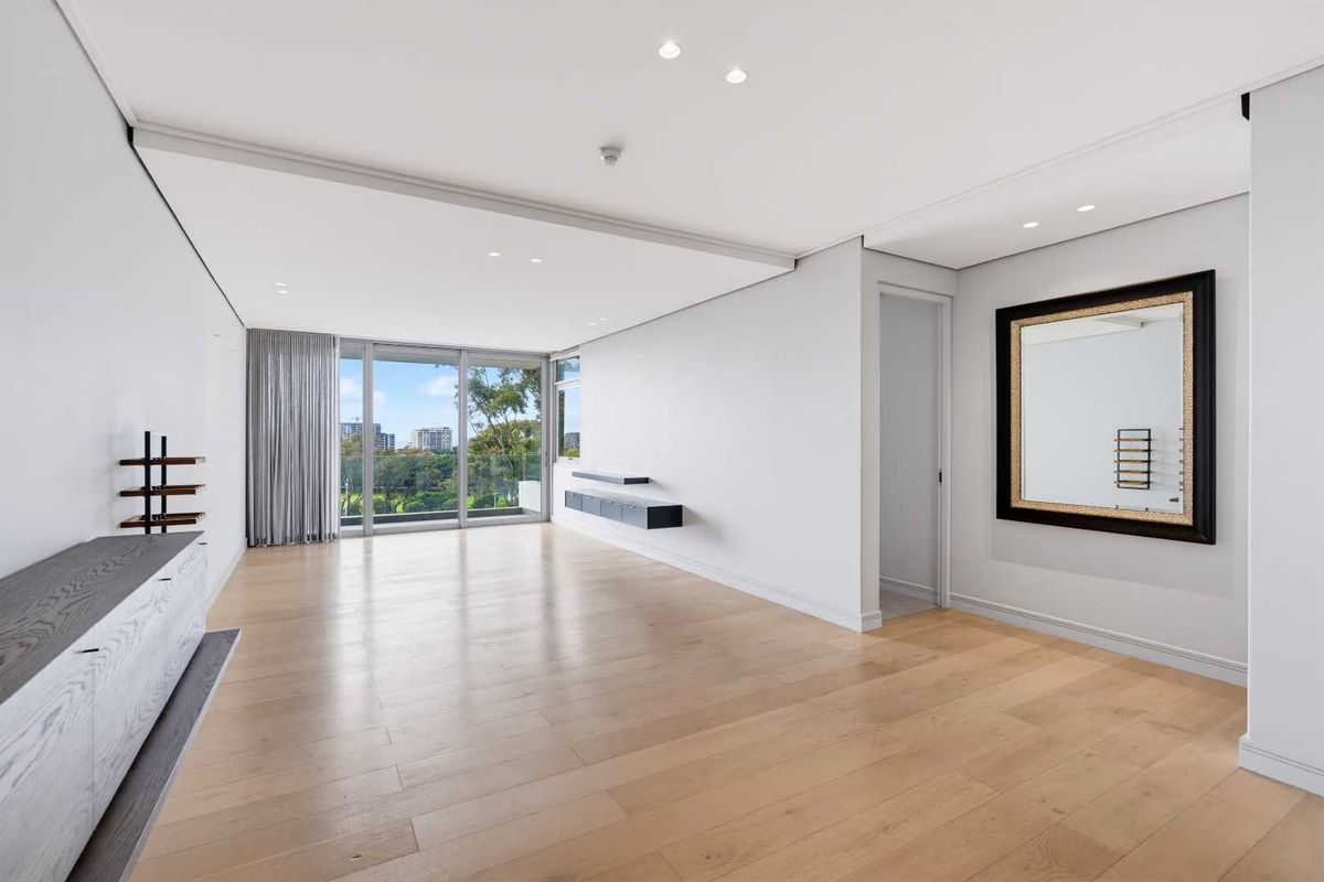 Spacious, light-filled living area featuring modern timber flooring, recessed lighting, and large sliding glass doors opening to a balcony with scenic views.