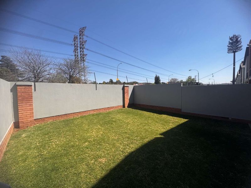 A private, enclosed garden area featuring a well-maintained lawn, brick boundary walls, and integrated electric security fencing.