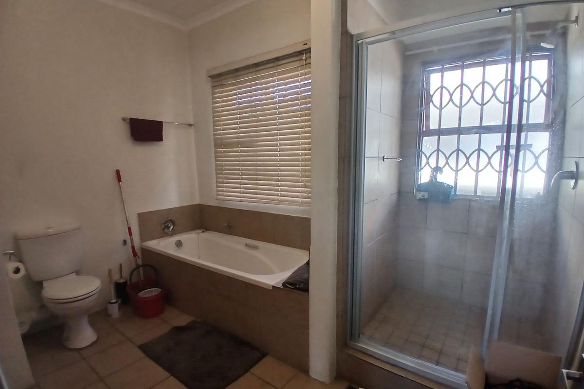 A functional bathroom featuring a built-in bathtub, a separate glass-enclosed shower, and a standard toilet with tiled flooring and window blinds.