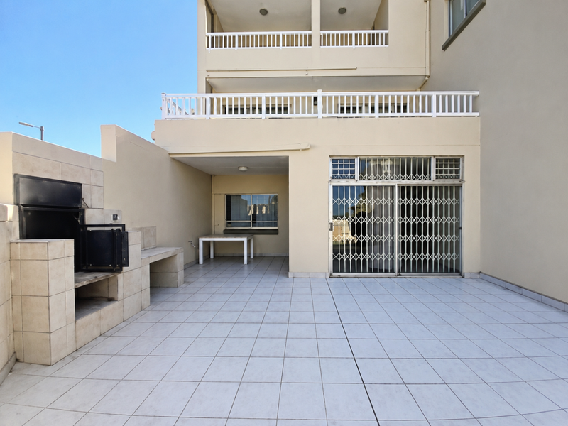 Spacious ground floor patio featuring a built-in braai, tiled flooring, and secure sliding door access to the interior living area.