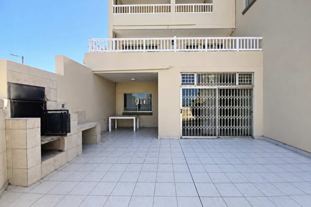 Spacious ground floor patio featuring a built-in braai, tiled flooring, and secure sliding door access to the interior living area.