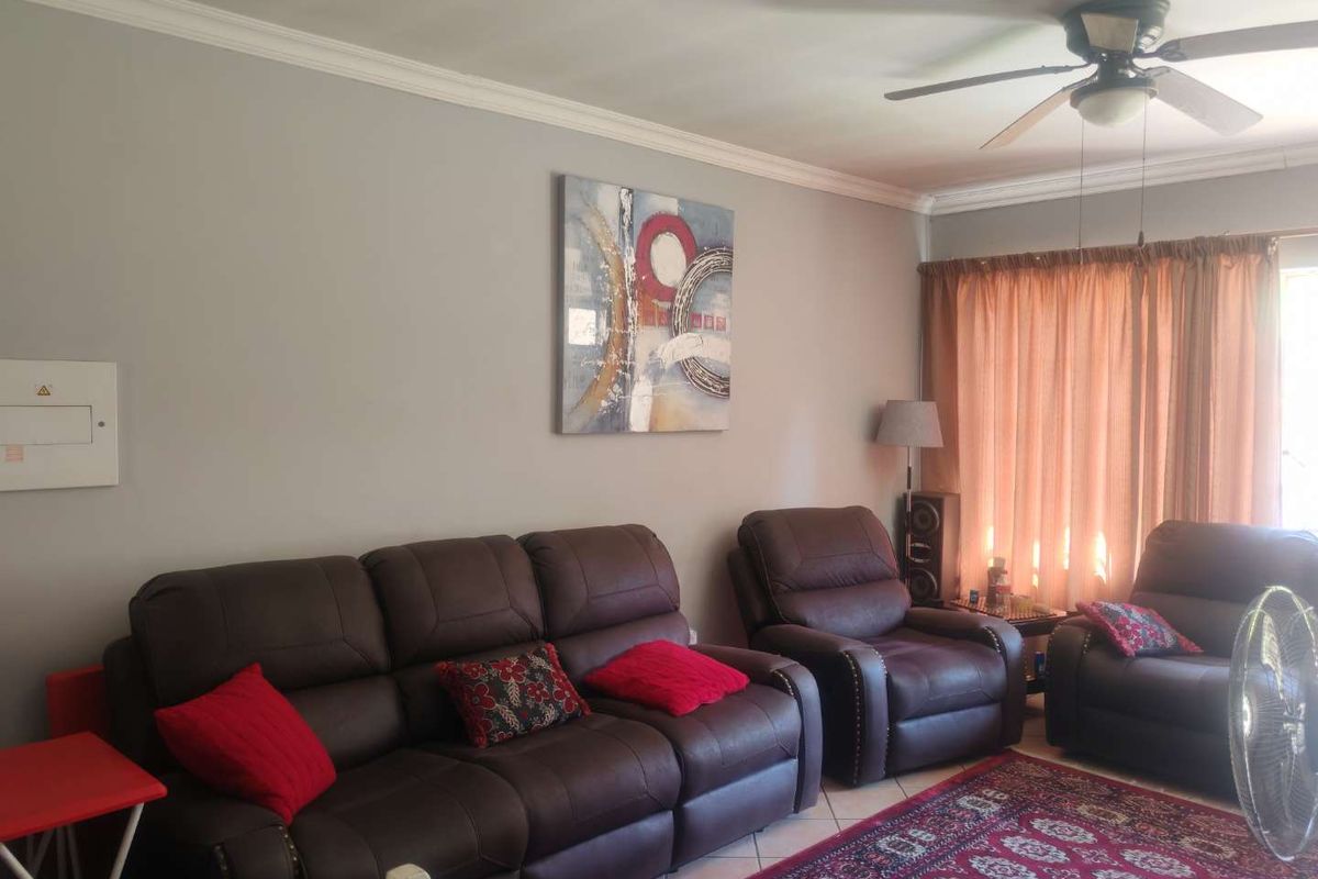 A comfortable living room featuring tiled flooring, crown molding, and a ceiling fan, providing a functional and well-lit space for relaxation.