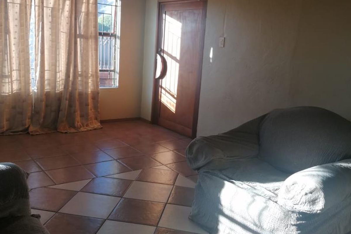 A living room featuring tiled flooring, a wooden entrance door, and natural light entering through a window with security bars.