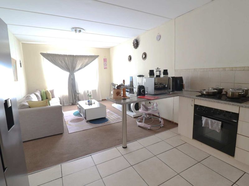 Open-plan living area featuring a functional kitchen with built-in oven, hob, and breakfast bar, seamlessly flowing into the carpeted lounge space.