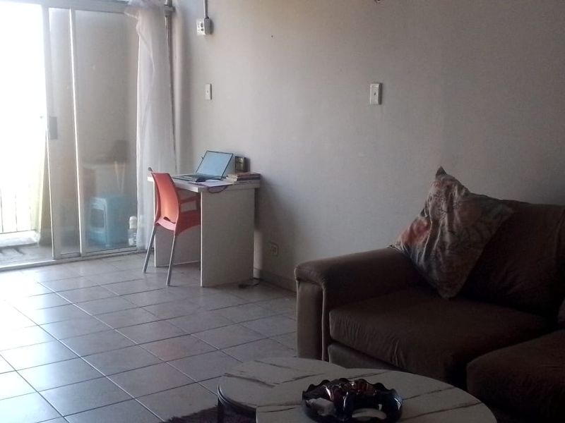 A living room area featuring tiled flooring and a large sliding glass door providing access to an outdoor balcony.