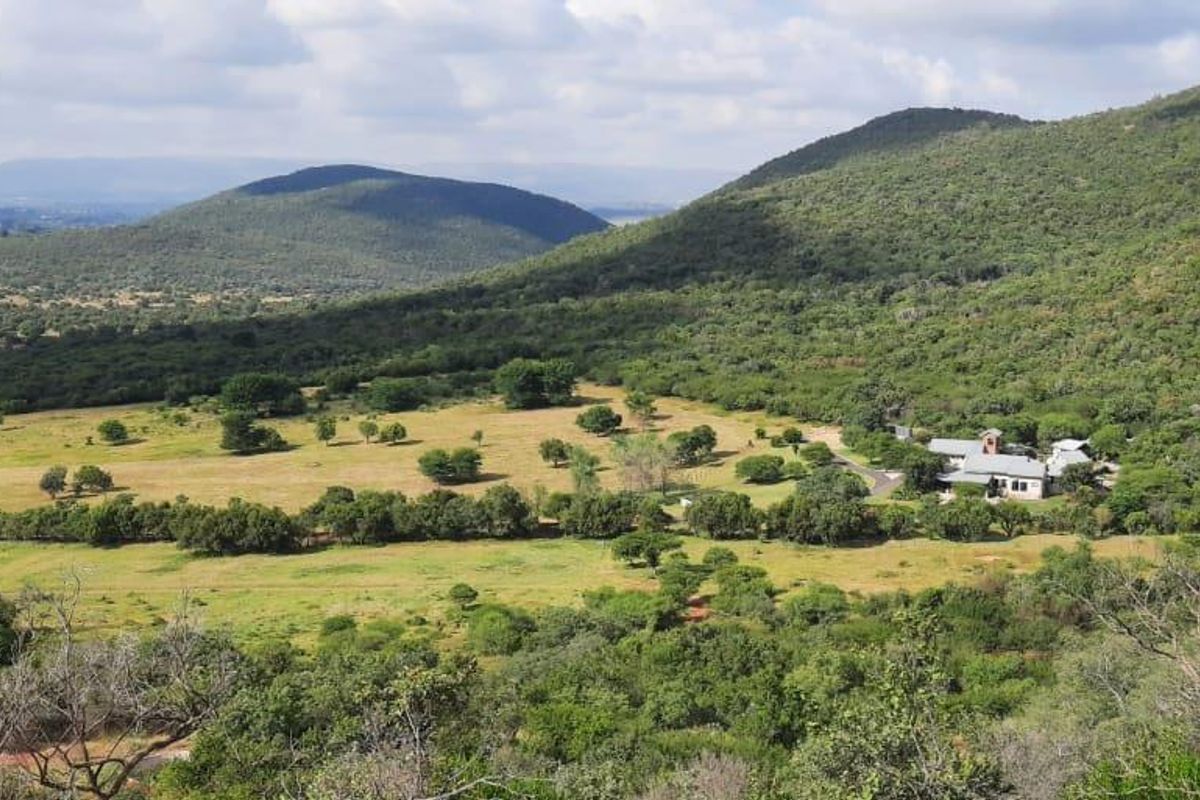 An elevated aerial view of a sprawling farm property set within a scenic, hilly rural landscape with extensive natural vegetation.