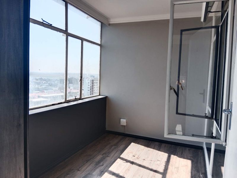 An enclosed balcony or sunroom featuring large steel-framed windows with city views and durable laminate flooring.