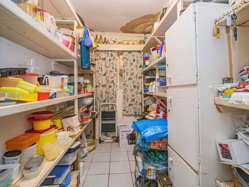 A functional scullery or pantry area featuring extensive built-in shelving and cabinetry, currently showing signs of ceiling water damage and wall wear.