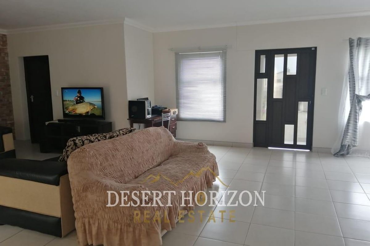 Spacious living room featuring neutral tiled flooring, a stone accent wall, and a modern front entrance door with glass panels.