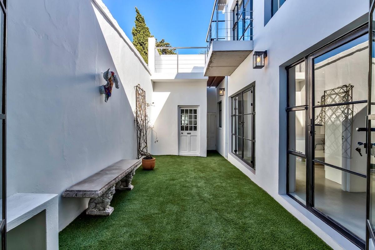 A private, enclosed courtyard featuring artificial turf, modern black-framed glass doors, and a balcony overlooking the space.