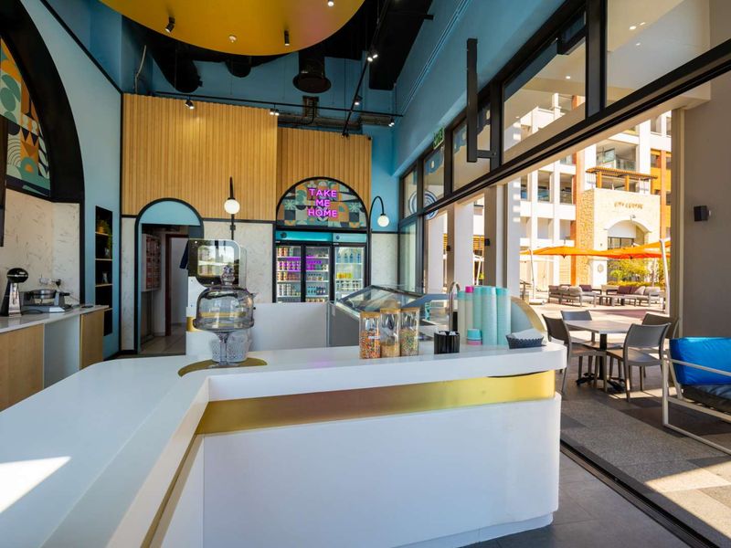 Modern open-plan commercial space featuring a sleek service counter, commercial refrigeration, and large sliding glass doors opening to an outdoor seating area.